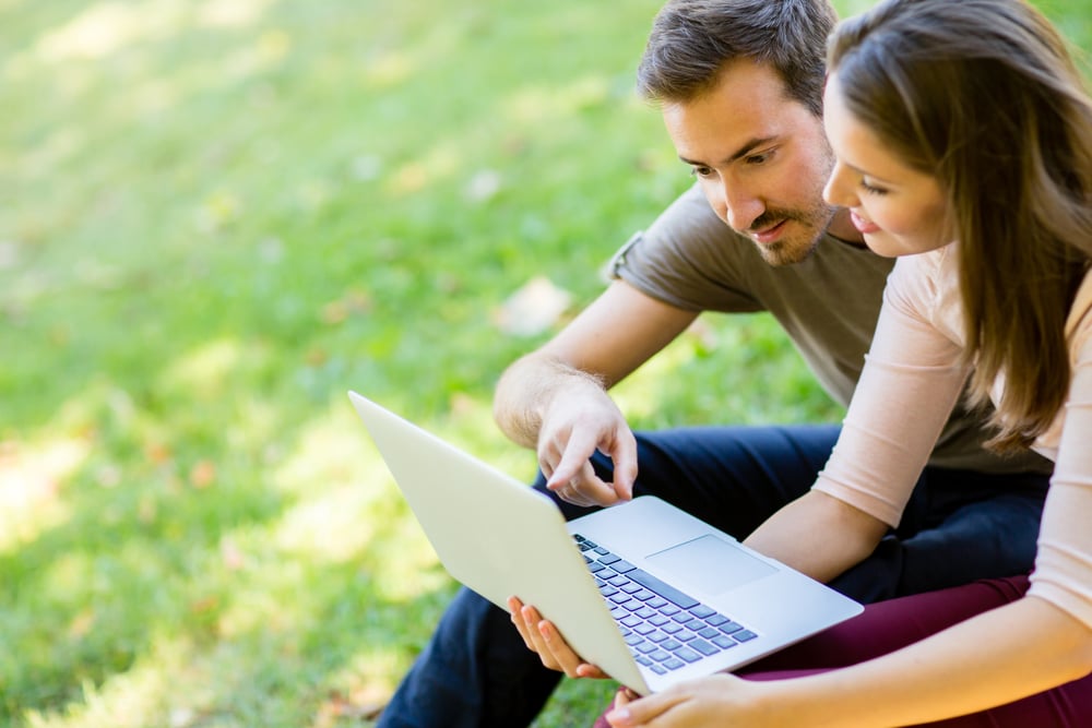 Couple using a laptop outdoors and looking happy